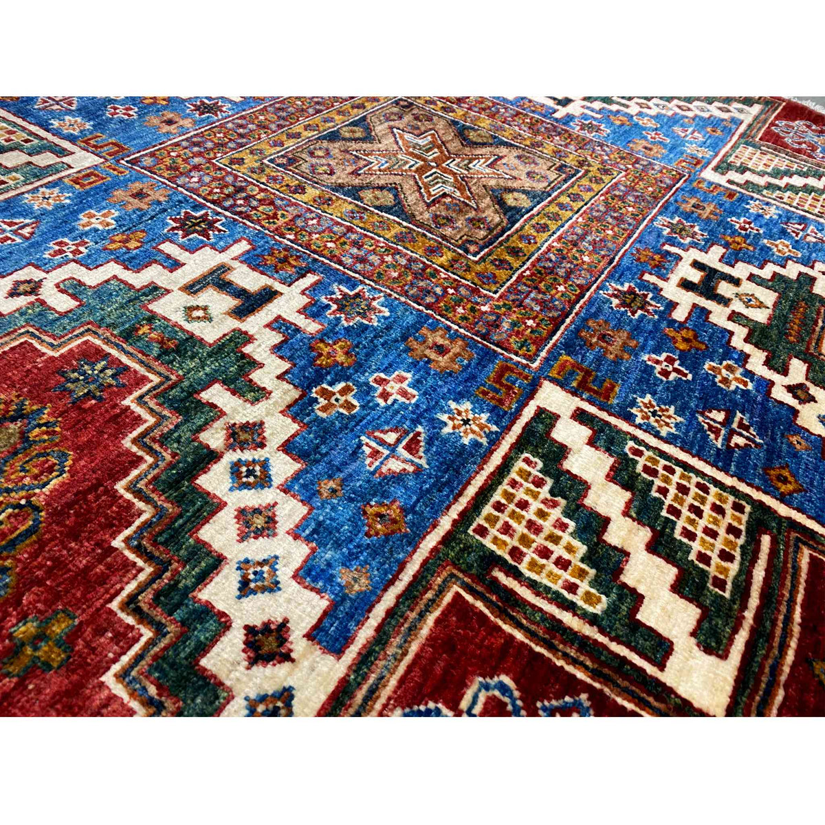 Detailansicht: blaues, rotes und cremefarbenes Zacken- und Kreuzmuster im Teppich