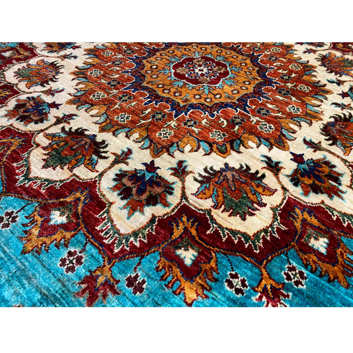 Detailansicht des Teppichmusters: türkise Fläche mit rotem, braunem und cremefarbenem Ornament.
