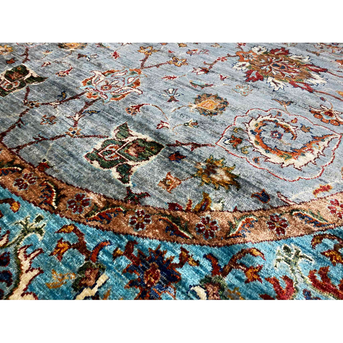 Teppich-Detail: grauer Flor mit bunten Ornamenten, goldbrauner Frieszone und türkiser Bordüre