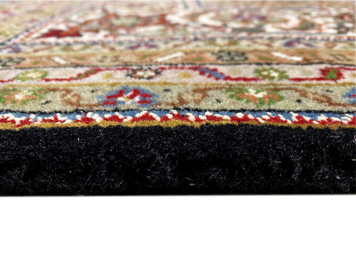 Nahaufnahme: Brauner Indo-Tabriz Teppich mit buntem Ornamentstreifen und Fransen.