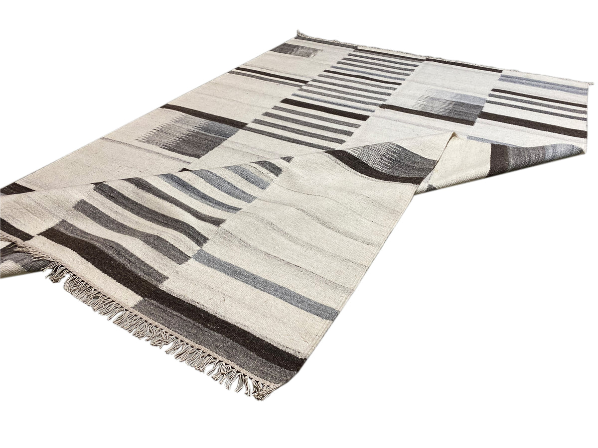 Kelim-Teppich mit Patchwork-Blocks und Linien in Creme, Grau und Blau, ausgefranste Kanten.