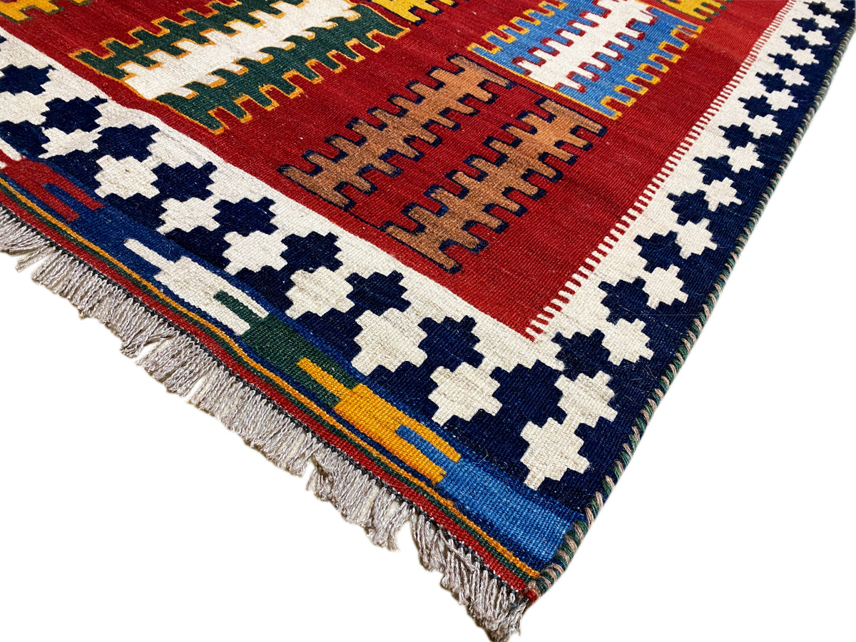 Kelim Teppich aus der Ecke: rotes Feld, blau-weiße Kreuzmotive und mehrfarbiger Randfries