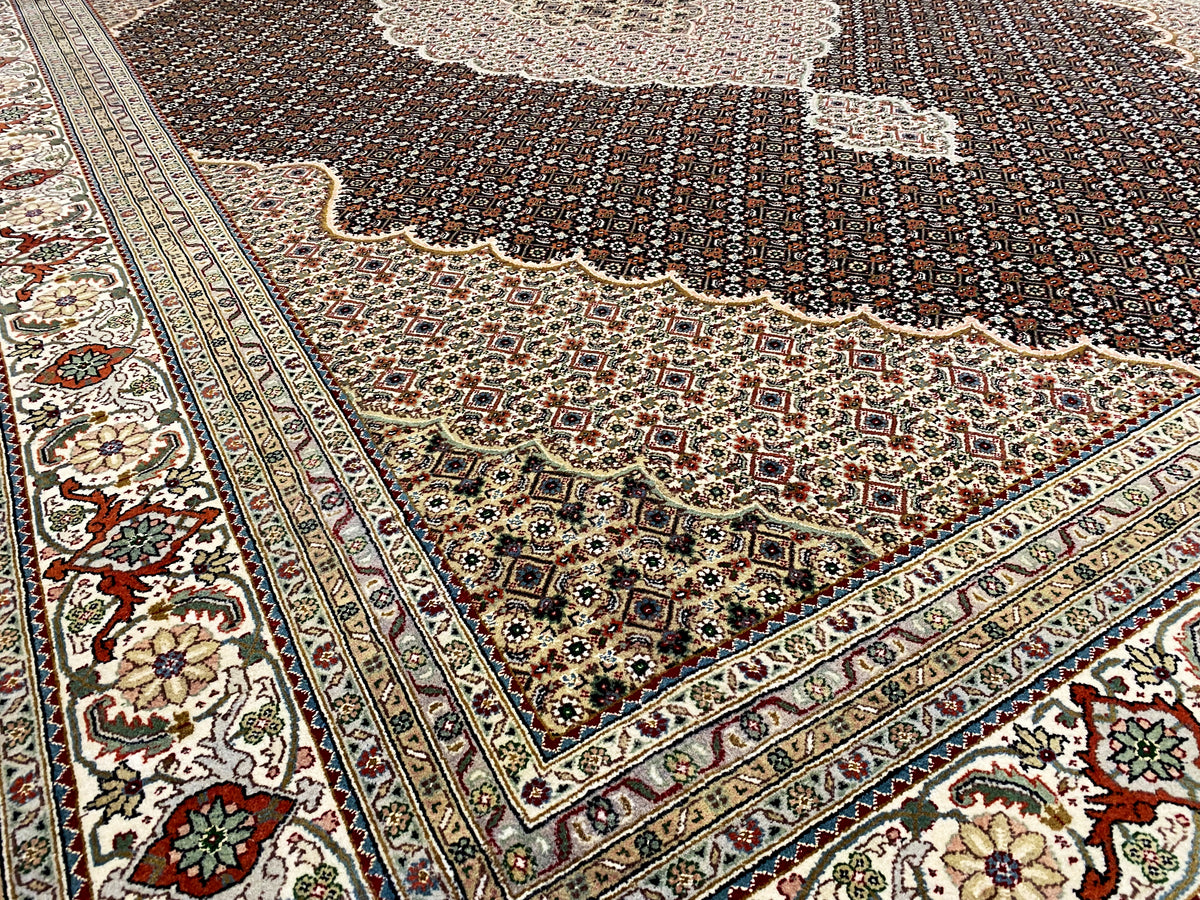 Ecke eines dunkelbraunen Teppichs mit Ornamentbordüre und floralen Details