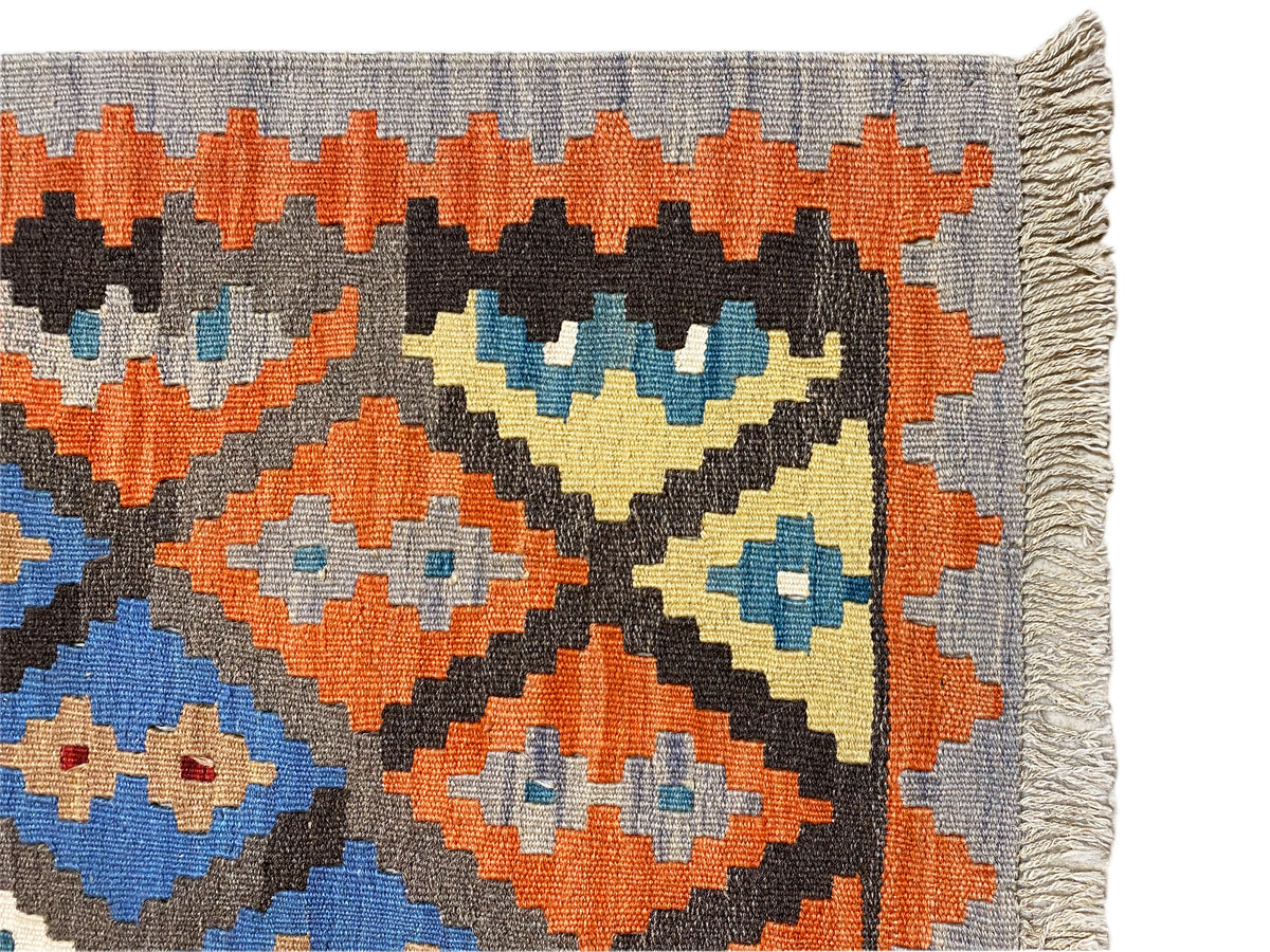 Detailansicht Kelim-Teppich: orange, blau und creme Rauten auf grauem Grund, ausgefranste Kanten