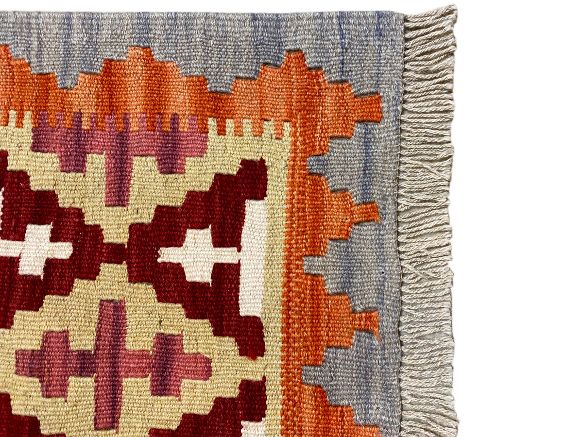 Detail vom Kelim-Teppich: Randfransen und Muster in Orange, Creme und Dunkelrot auf Grau