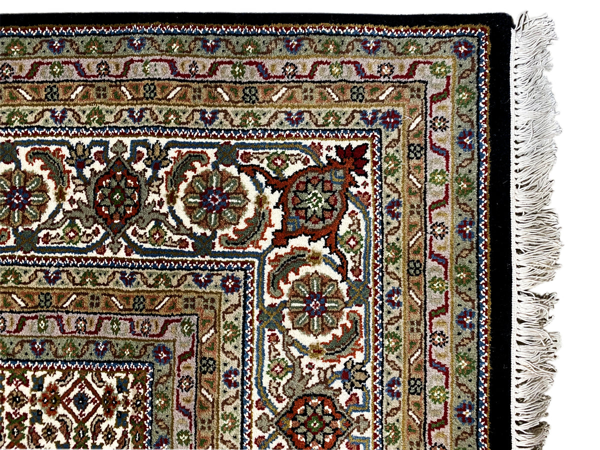 Nahaufnahme der Bordüre eines braunen Indo-Tabriz Teppichs mit floralen Ornamenten und Fransen.