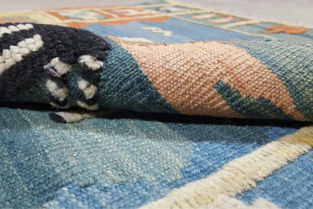 Nahaufnahme: gewebter Kilim mit blauem und beigem Flor sowie orange-braunen Akzenten
