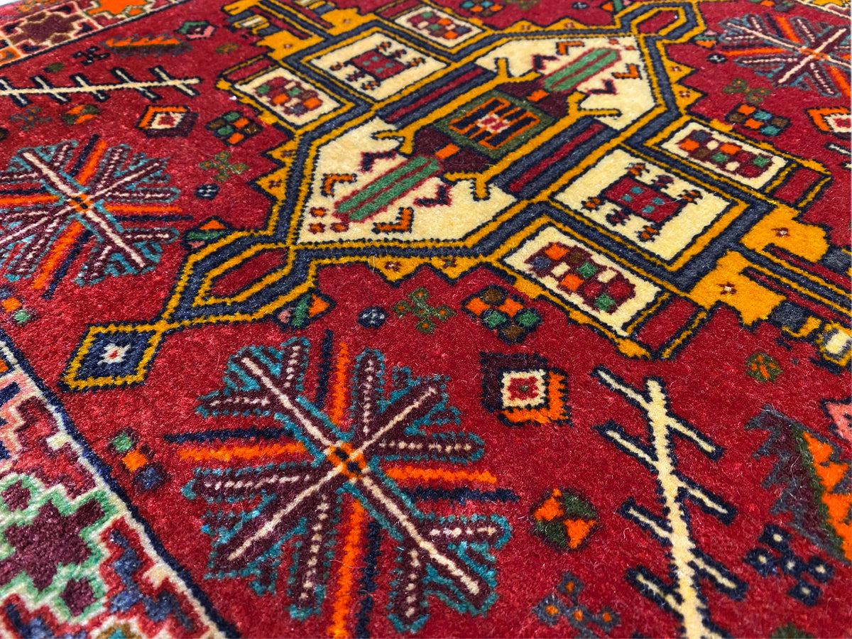 Nahaufnahme: Poshti Teppich mit rotem Hintergrund und bunten geometrischen Motiven