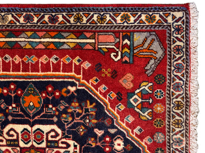 Teppich-Detail: rotes und blaues Ornamentfeld mit mehrfarbiger Bordüre und Fransen
