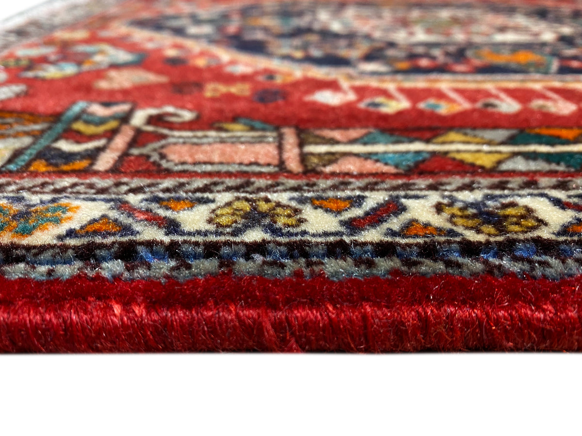 Teppichkante im Detail: roter Flor, mehrfarbige Musterborte und ausgefranste Fransen