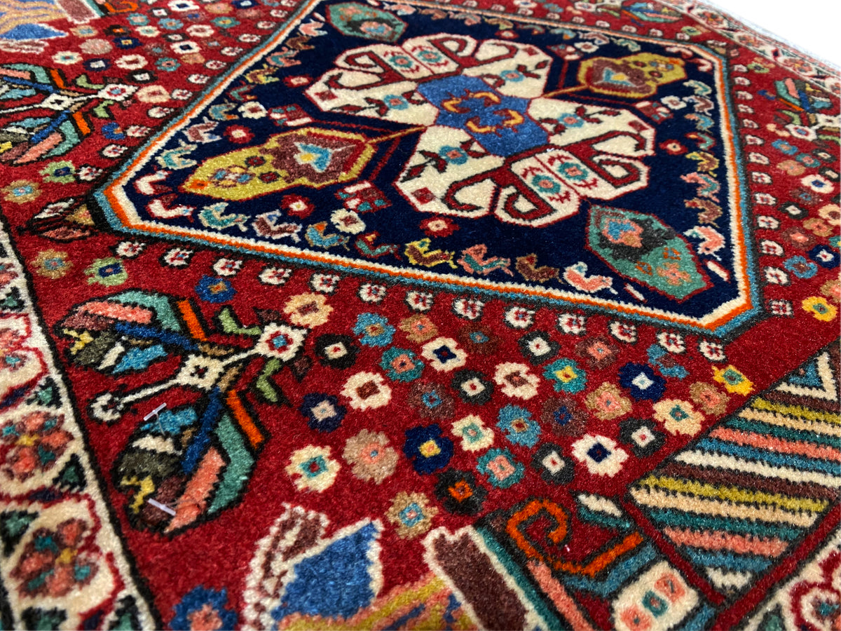 Teppichdetail: bunte Rauten und Blumenmuster auf rotem Grund