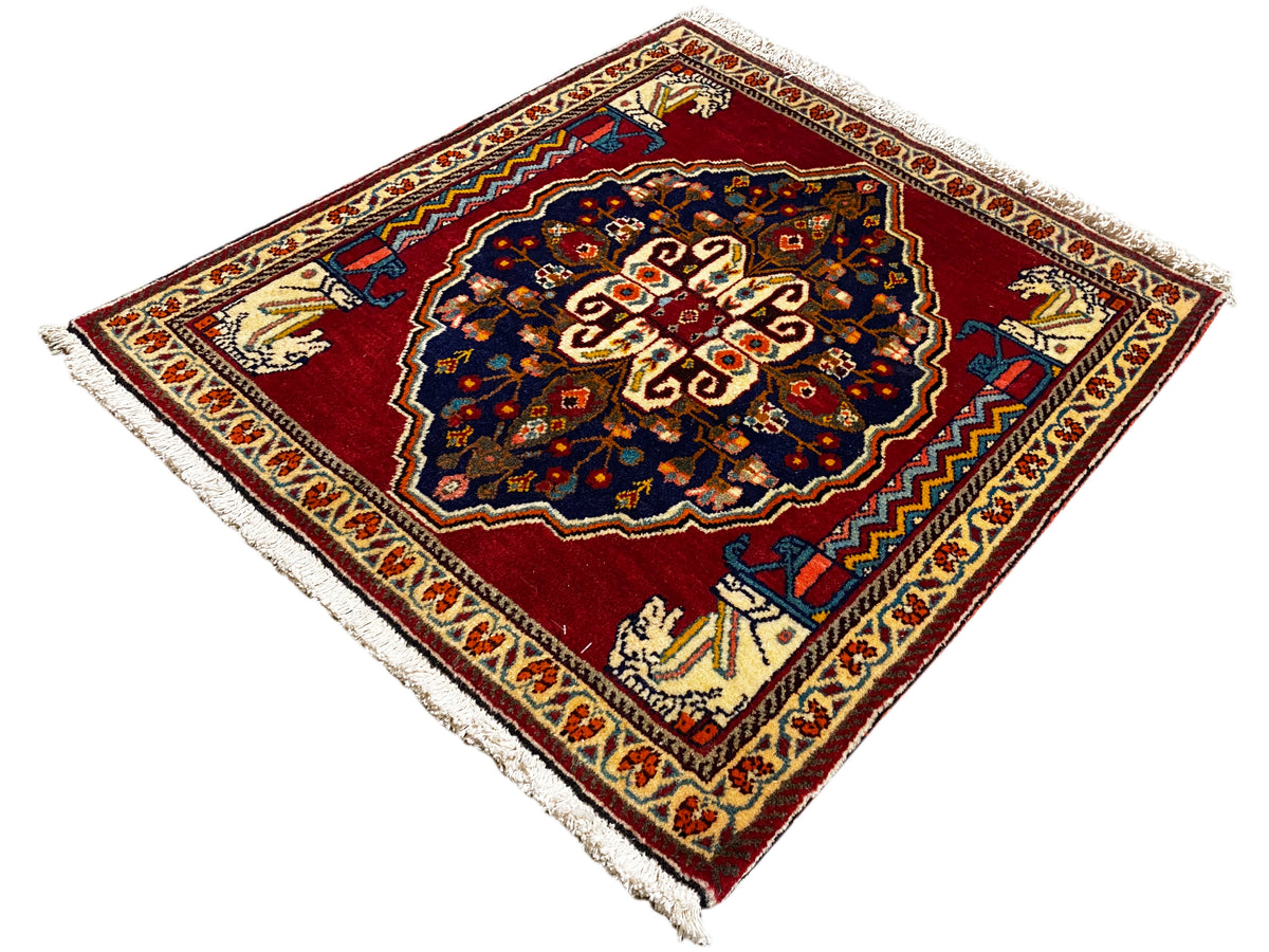 Teppich mit rotem Grund, dunkelblauem Mittelmotiv, beigen Ornamentleisten und Fransen