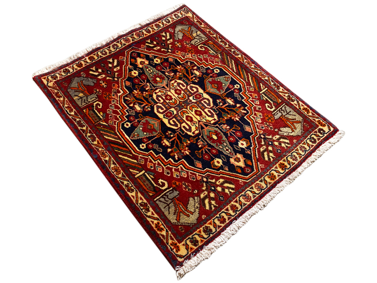 Teppich 65x59 cm als gedrehte Ansicht: roter Rand, dunkle Muster, seitliche Fransen