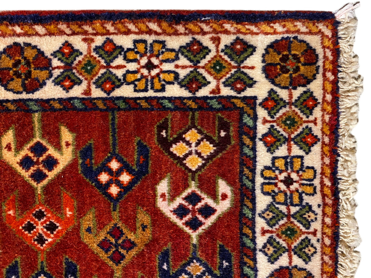 Teppich-Detail: rote Fläche mit Ornamentborte, bunten Rauten und ausgefransten Seitenkanten