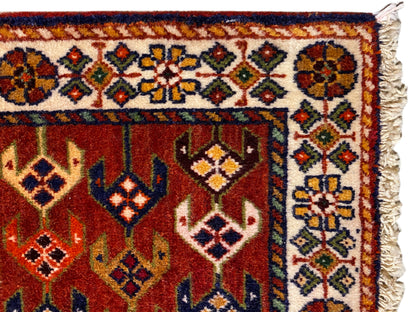Teppich-Detail: rote Fläche mit Ornamentborte, bunten Rauten und ausgefransten Seitenkanten
