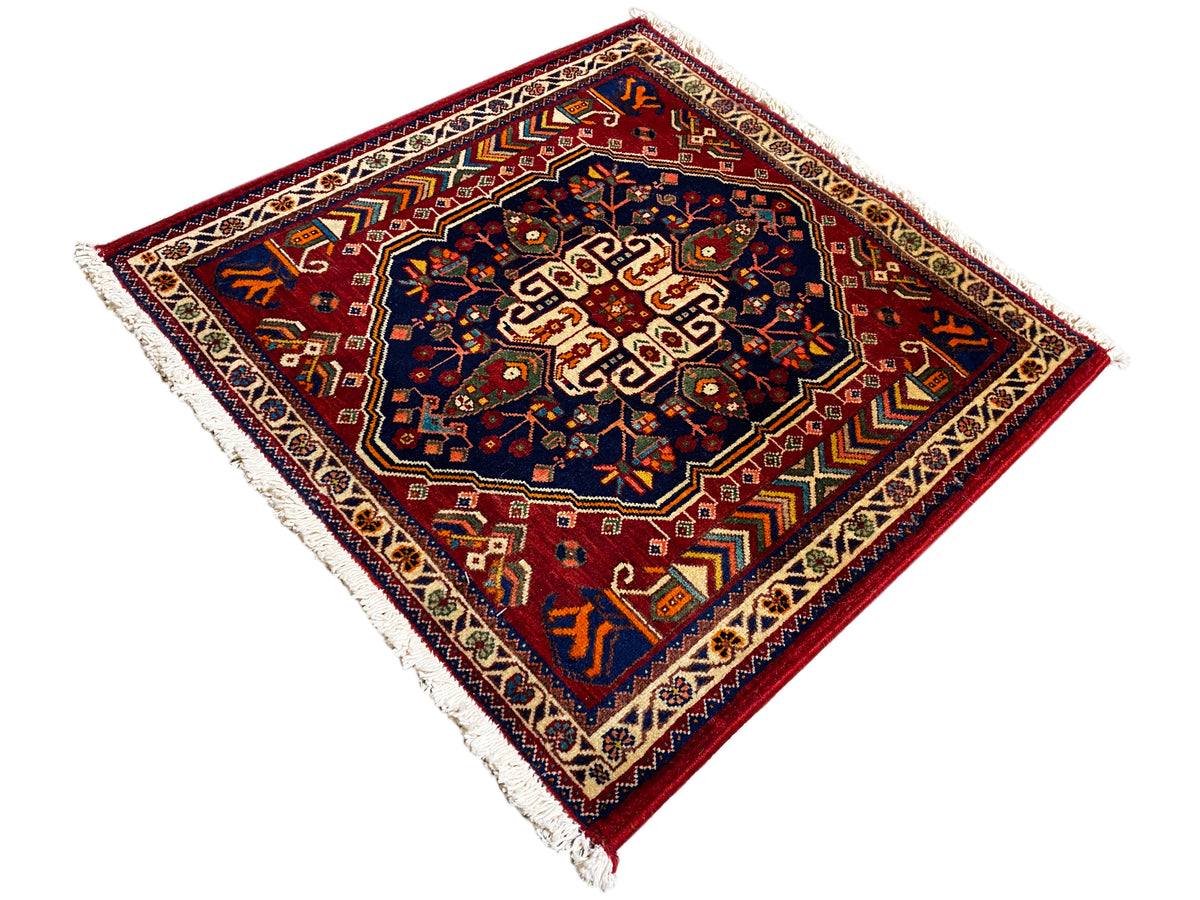 Teppich 63x60 cm mit diagonaler Ansicht: dunkelblaues Zentrum, roter Rand, Fransen