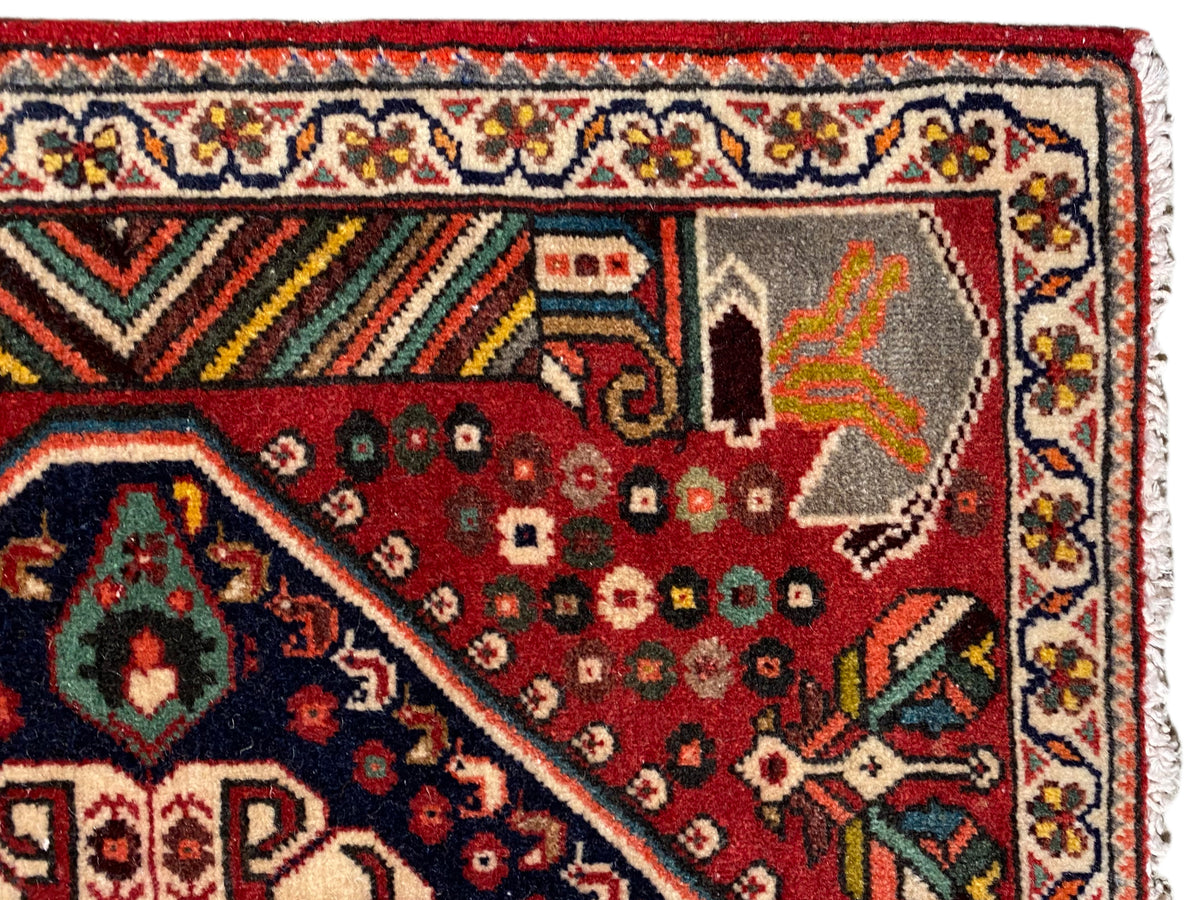 Detailansicht: roter Teppich mit ornamentalen Motiven, mehrfarbiger Bordüre und Fransen