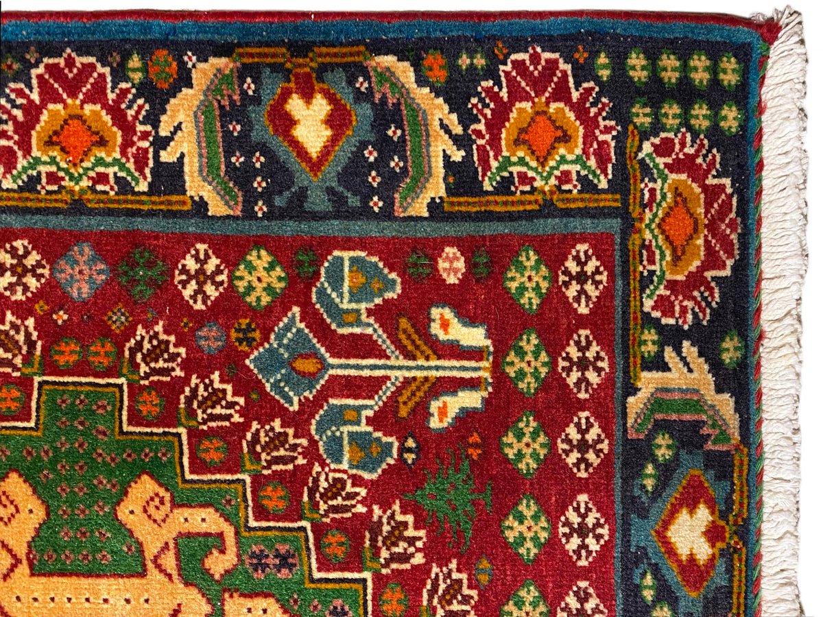 Teppich detailnah: farbenfrohe Ornamente auf dunklem Grund, rote und grüne Motive, gewebter Rand