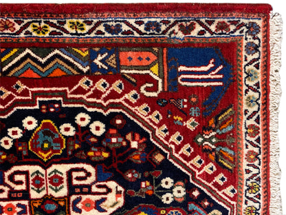 Detailansicht vom Teppich: roter Hintergrund, dunkelblaues Feld, Ornamente und Bordüre