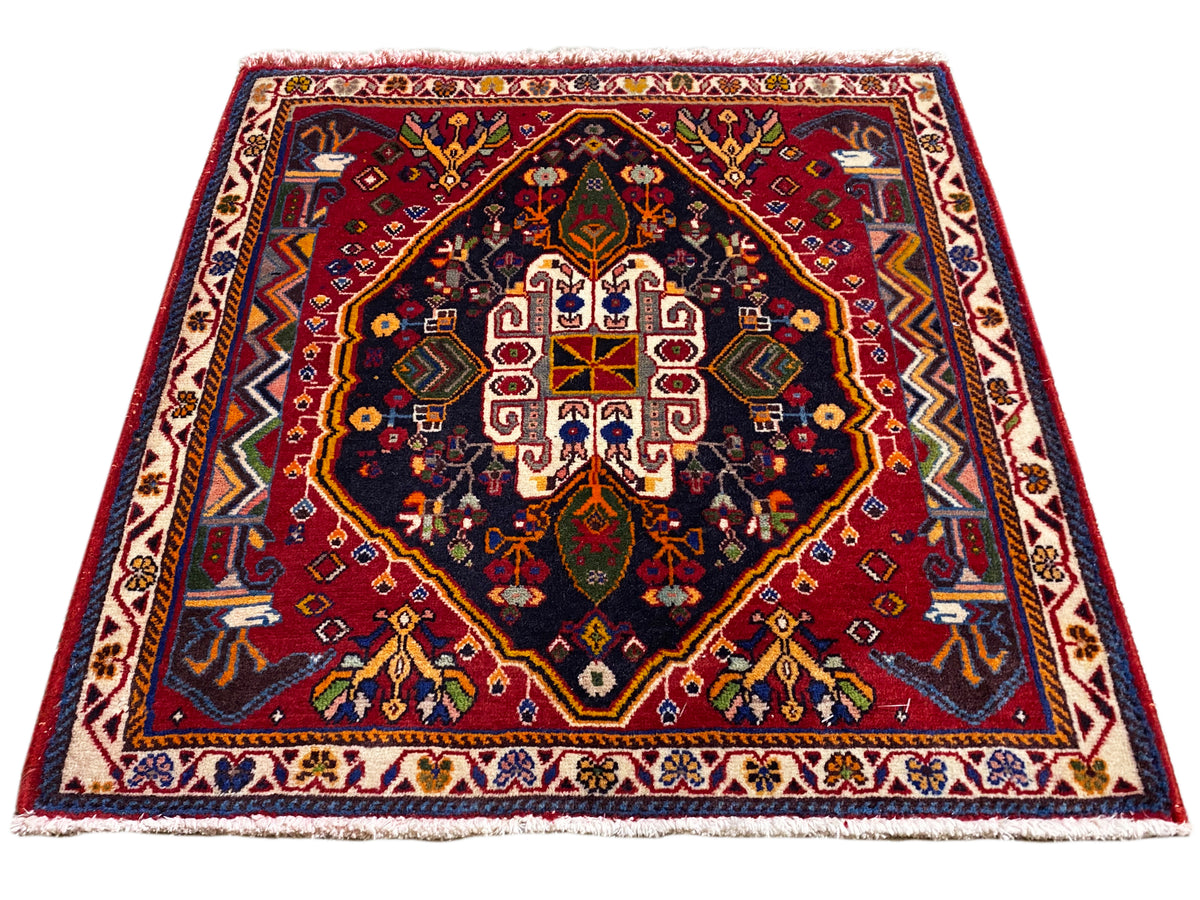 Poshti-Teppich (67×67 cm) im Schrägbild: Bordüre, rotes Zentrum, dunkles Blau
