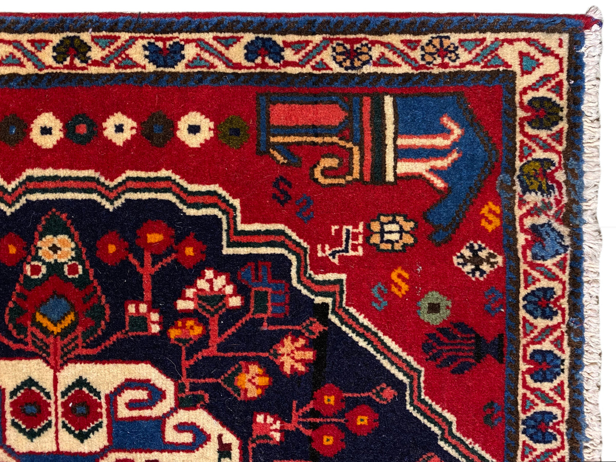 Teppich-Ecke mit rotem Grund, farbigen Symbolen und blauem Zierrahmen
