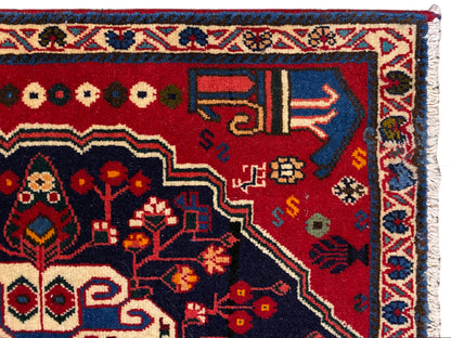 Teppich-Ecke mit rotem Grund, farbigen Symbolen und blauem Zierrahmen